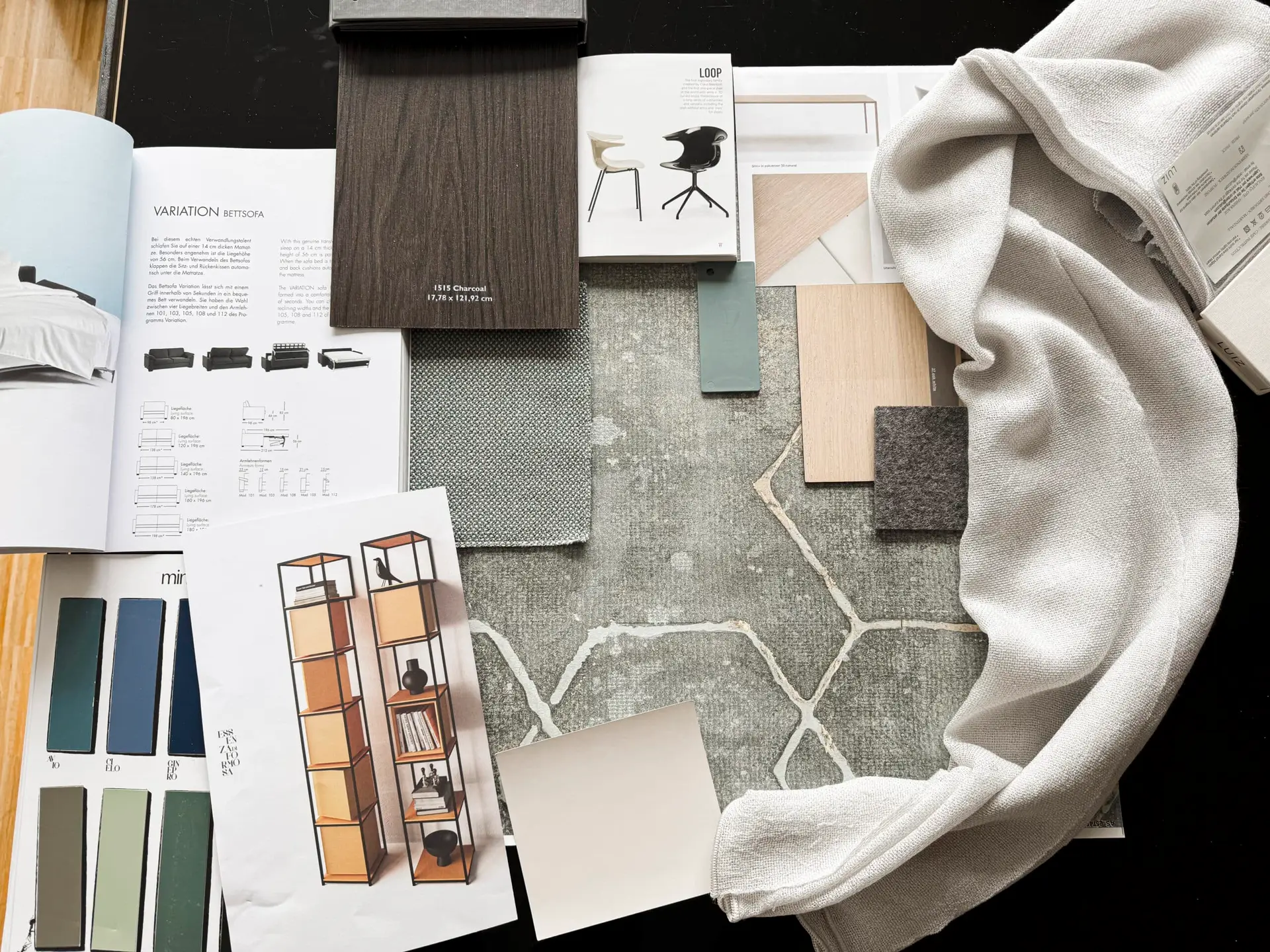 Eine Auswahl an Designmaterialien und -mustern, darunter Stoffproben, Holzmuster, Farbpaletten und Möbelkataloge, die ausgebreitet auf einem Tisch liegen.