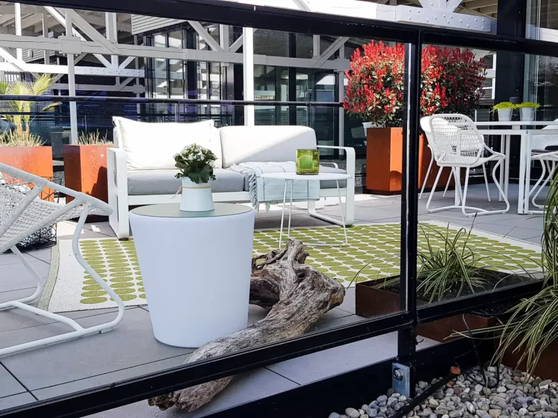 Eine Terrasse mit weißen Gartenmöbeln, einem weißen Teppich mit grünen Punkten, Pflanzgefäßen und Dekoration.